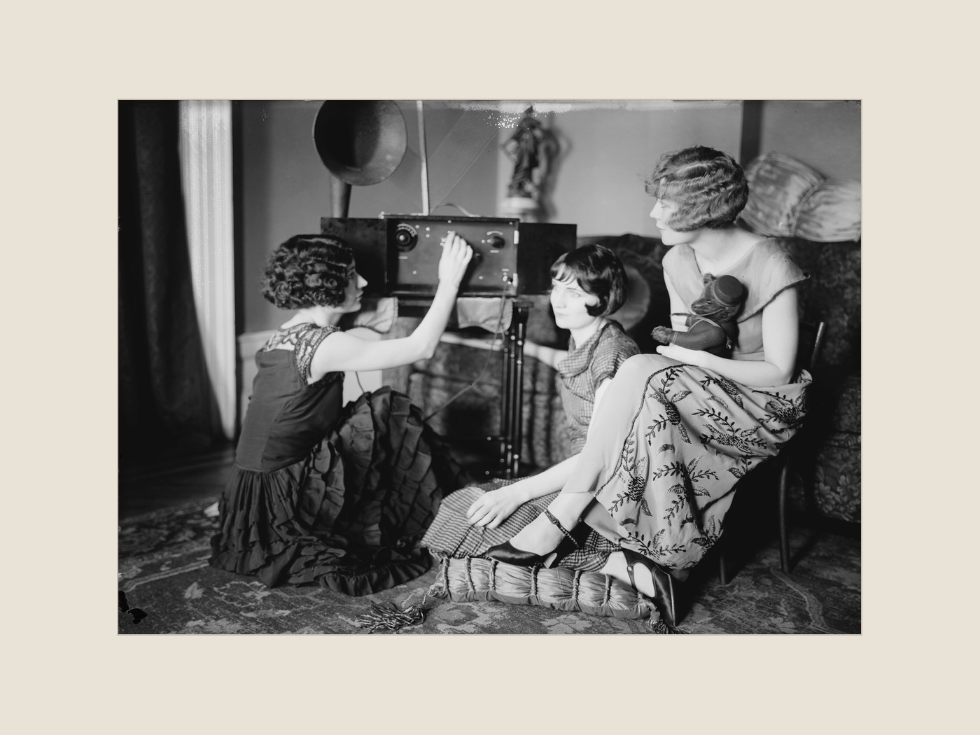 1920 年代客厅里三位年轻女性围着一台收音机，机身上方是喇叭形扬声器